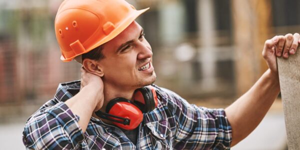 Be careful. Construction worker in protective helmet feeling neck pain while working at construction site. Building construction. Pain concept. Dangerous job
